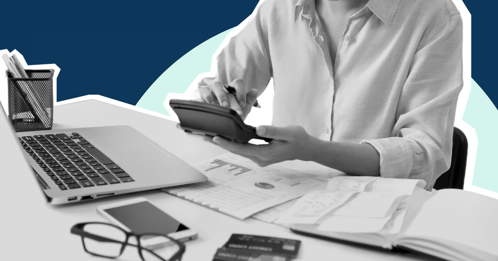 Person holding a calculator in front of a desk with papers and laptop.