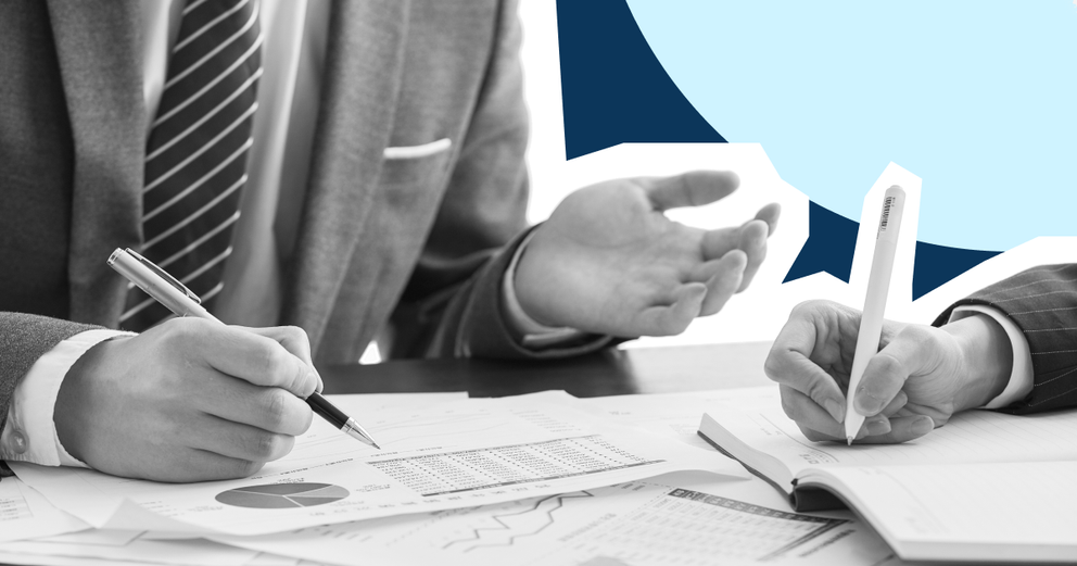 A couple of hands holding pens, on top of paper of pie charts and statistics.