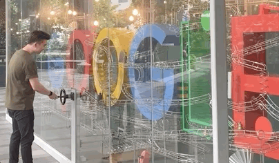 A visitor turning a crank on a glass-cased kinetic sculpture spelling Google in its brand colours