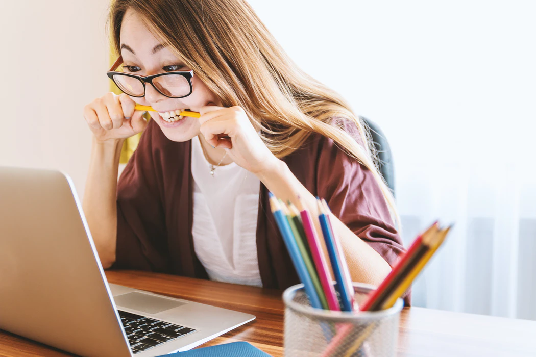 A stressed woman bites her pencil while looking at her laptop