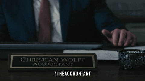 A desk nameplate reading Christian Wolff, Accountant, with someone typing behind it