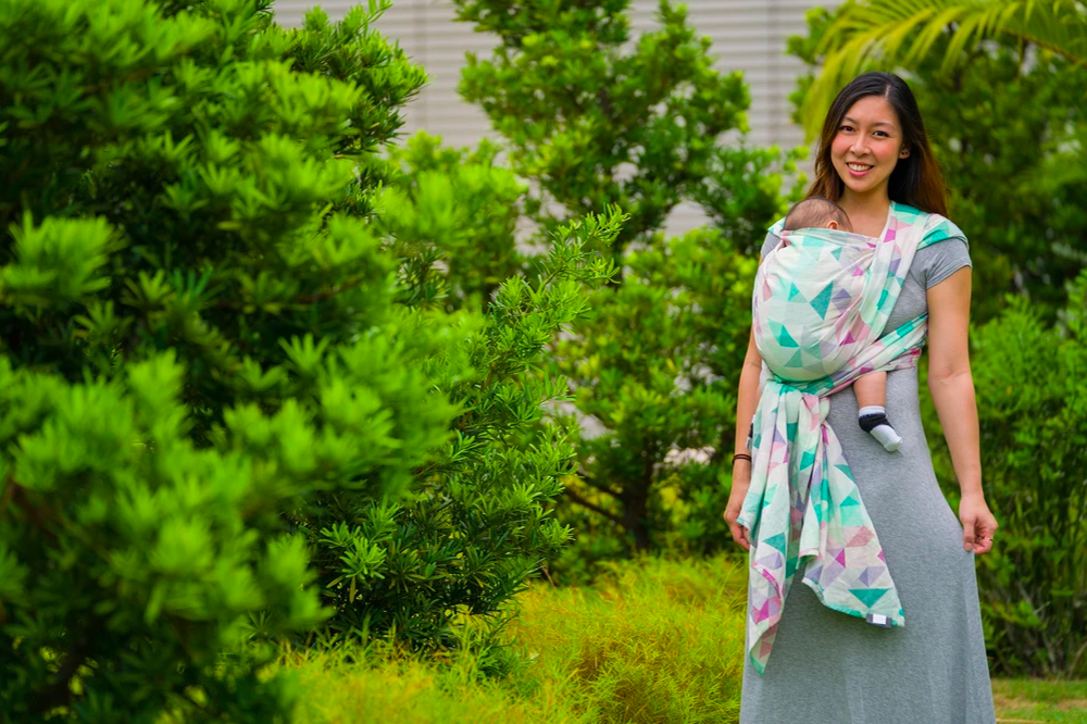 A woman outdoors carrying a baby against her chest in a patterned woven wrap