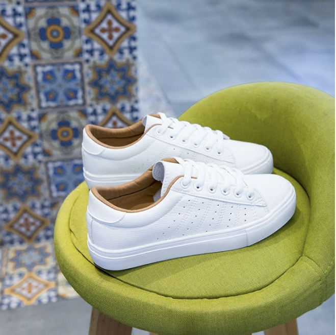 A pair of plain white leather lace-up sneakers on a green upholstered stool