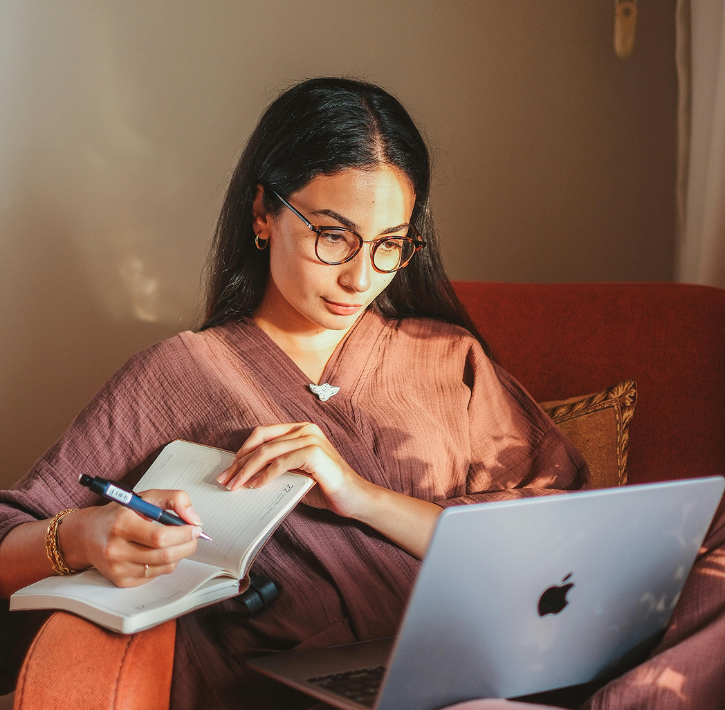 A person working at a laptop with an open notebook beside them